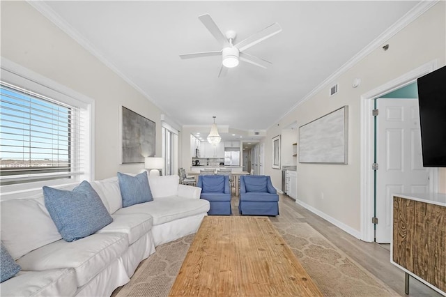 living area with visible vents, ornamental molding, light wood-type flooring, baseboards, and ceiling fan