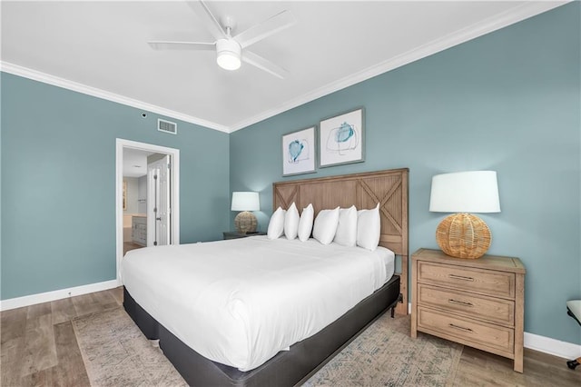 bedroom featuring wood finished floors, visible vents, ensuite bath, crown molding, and baseboards
