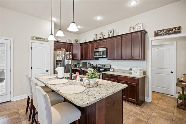 kitchen featuring dark brown cabinetry, light stone counters, a breakfast bar, decorative light fixtures, and stainless steel appliances