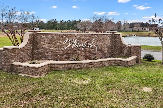 community / neighborhood sign featuring a water view and a lawn