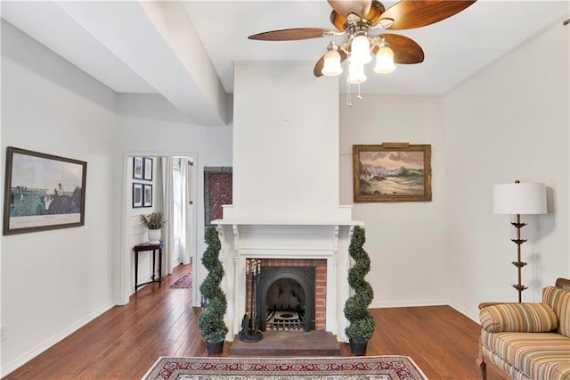 living room featuring a brick fireplace, ceiling fan, and dark wood-type flooring