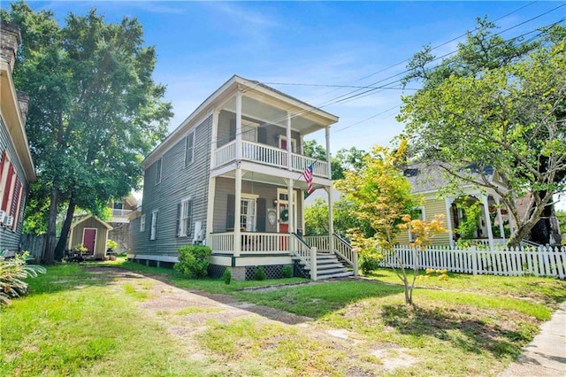 view of front of house featuring a porch, a balcony, a front yard, and a storage shed