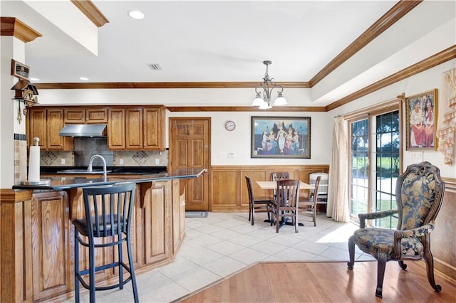 kitchen with kitchen peninsula, a kitchen breakfast bar, decorative light fixtures, ornamental molding, and a chandelier