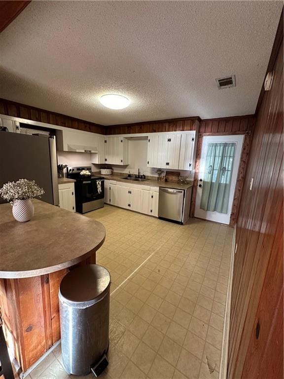 kitchen with a textured ceiling, stainless steel appliances, wooden walls, sink, and white cabinets