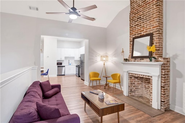 living room featuring ceiling fan, lofted ceiling, a fireplace, and light hardwood / wood-style floors