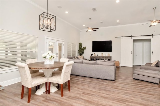 dining room featuring high vaulted ceiling, ceiling fan with notable chandelier, a barn door, and light wood-type flooring