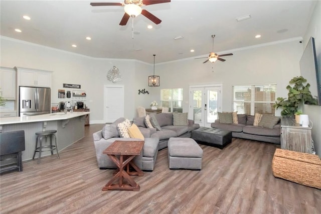 living room with light wood-type flooring, a towering ceiling, ceiling fan, and crown molding