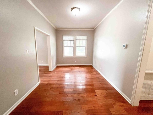 empty room with baseboards, wood finished floors, visible vents, and crown molding