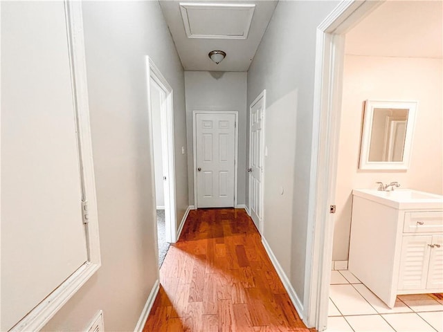 hall featuring a sink, light wood-style flooring, and baseboards