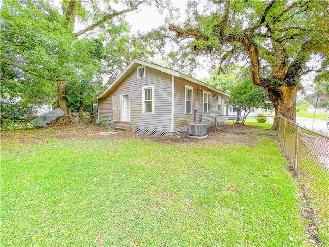 view of side of property featuring entry steps, a lawn, fence, and central air condition unit