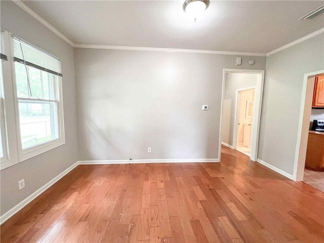 spare room featuring baseboards, ornamental molding, visible vents, and light wood-style floors