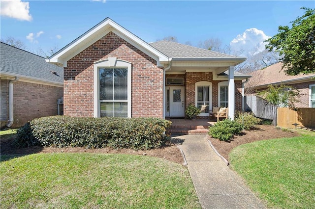 view of front of home featuring a shingled roof, brick siding, fence, and a front lawn