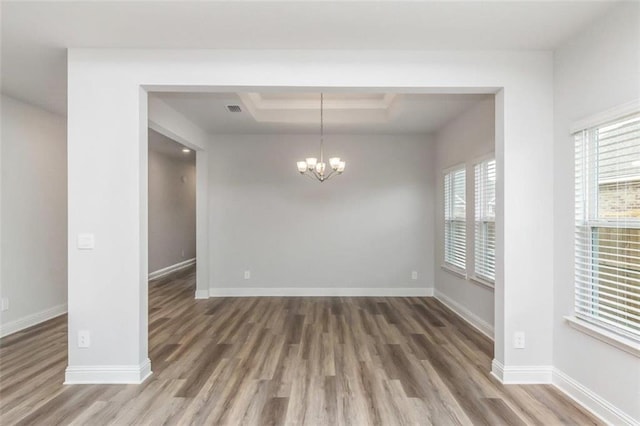 unfurnished dining area featuring a raised ceiling, an inviting chandelier, and dark hardwood / wood-style flooring