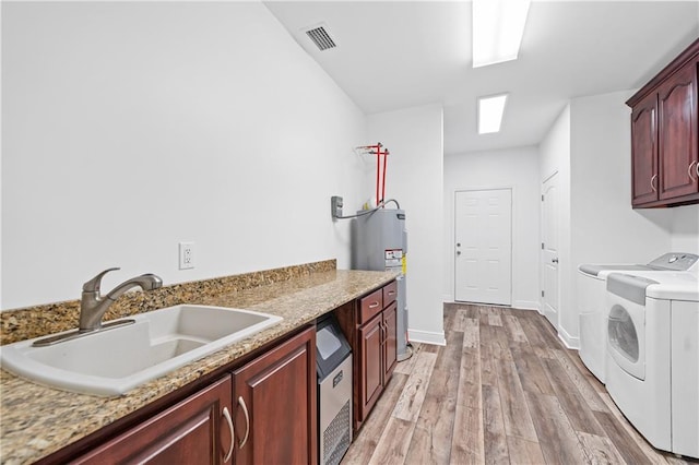 washroom featuring cabinets, sink, electric water heater, washer and clothes dryer, and light hardwood / wood-style flooring