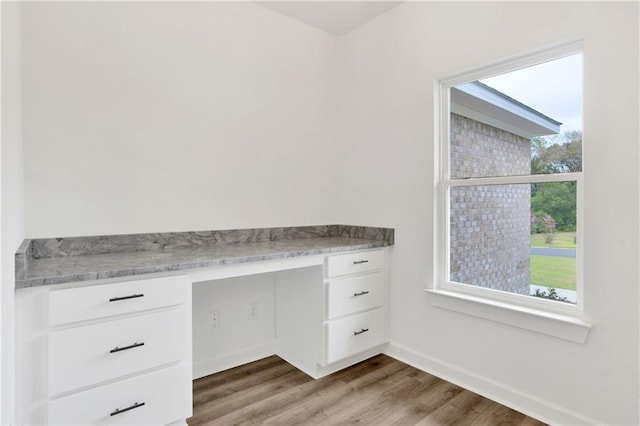 unfurnished office with wood finished floors, built in desk, and baseboards