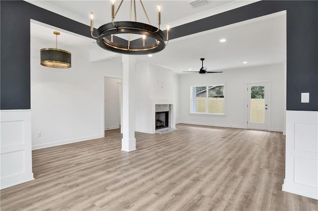 unfurnished living room with a high end fireplace, wainscoting, recessed lighting, ceiling fan with notable chandelier, and light wood-style floors