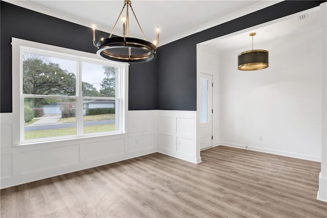 unfurnished dining area featuring light wood finished floors, ornamental molding, wainscoting, an inviting chandelier, and a decorative wall