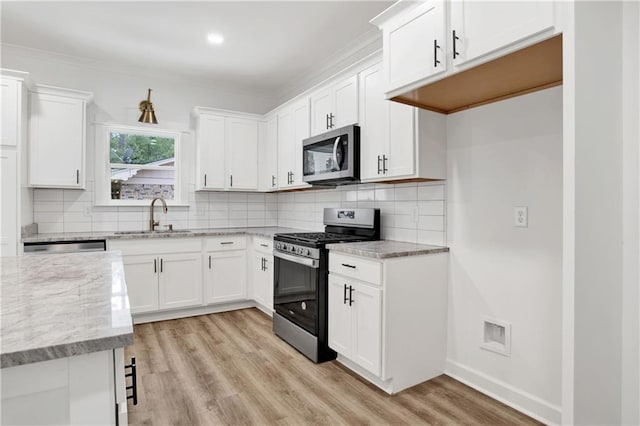 kitchen with light stone countertops, light wood-style flooring, appliances with stainless steel finishes, white cabinets, and a sink