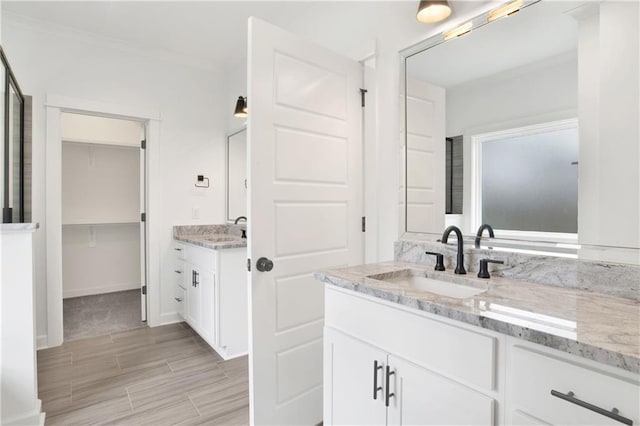 bathroom featuring ornamental molding, two vanities, baseboards, and a sink