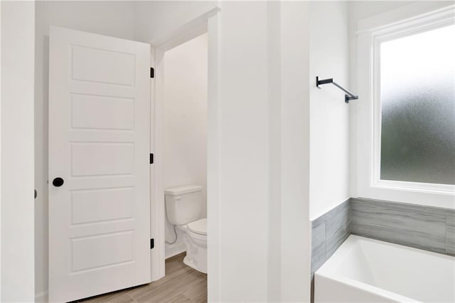 full bath with toilet, a bath, and wood finished floors