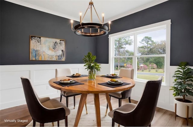 dining room with wood finished floors, a wainscoted wall, ornamental molding, a decorative wall, and a chandelier