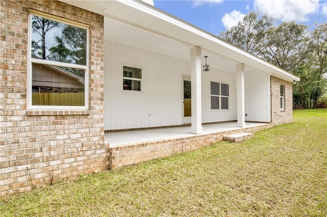 view of side of home featuring a yard, brick siding, and a patio