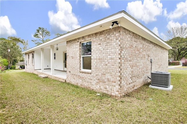 view of side of home featuring brick siding, a patio area, a lawn, and central AC