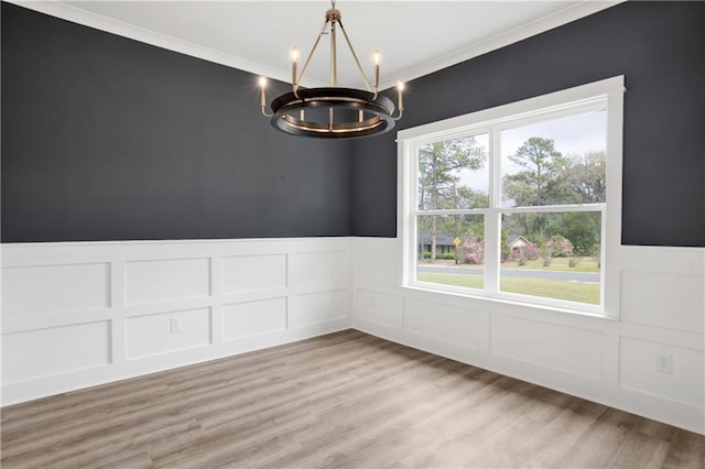 unfurnished room with light wood-type flooring, a notable chandelier, a decorative wall, wainscoting, and crown molding