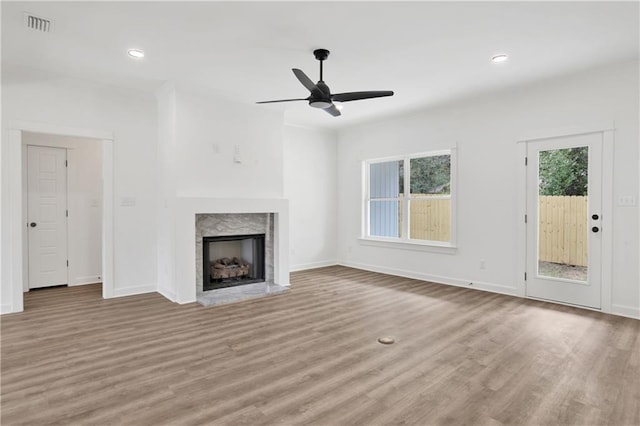 unfurnished living room with visible vents, baseboards, a premium fireplace, wood finished floors, and a ceiling fan