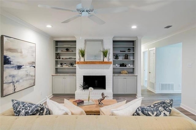 living room with ceiling fan, light wood-type flooring, a brick fireplace, built in features, and crown molding