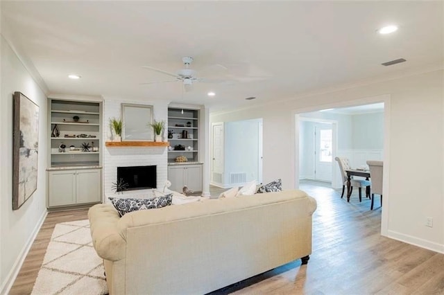 living room with a large fireplace, ceiling fan, crown molding, and light hardwood / wood-style flooring