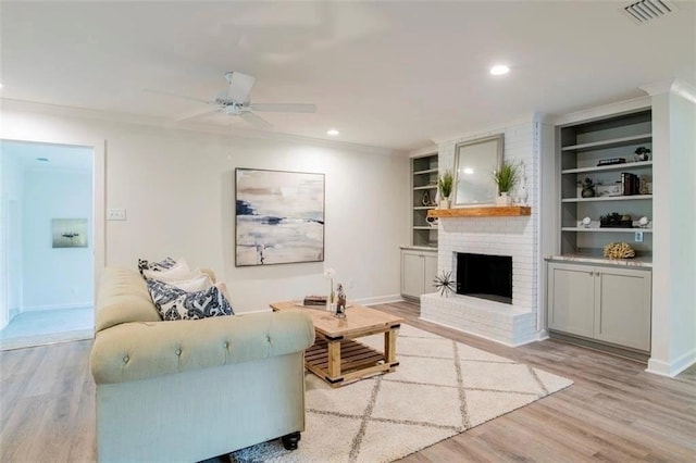 living room featuring ornamental molding, a brick fireplace, built in shelves, light hardwood / wood-style floors, and ceiling fan