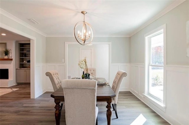 dining room with crown molding, dark hardwood / wood-style floors, a notable chandelier, and a brick fireplace