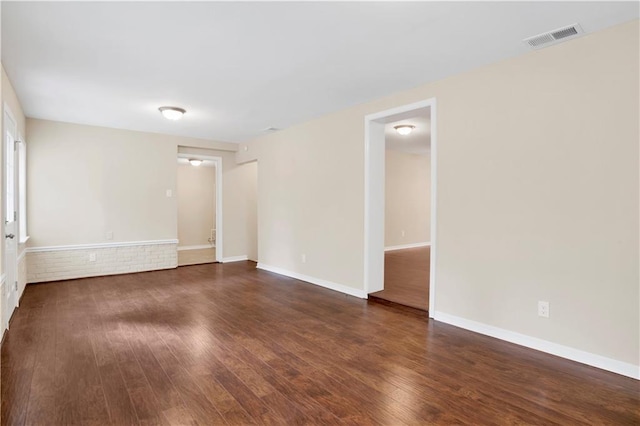 spare room featuring dark wood-style flooring, visible vents, and baseboards