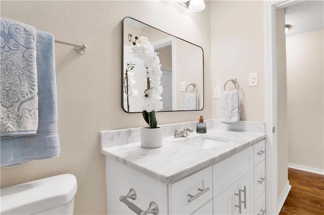 bathroom with toilet, wood finished floors, vanity, and baseboards