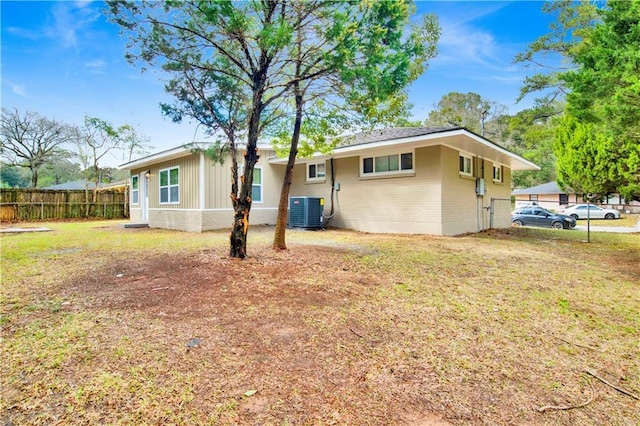 rear view of property with a lawn, fence, central AC, and brick siding