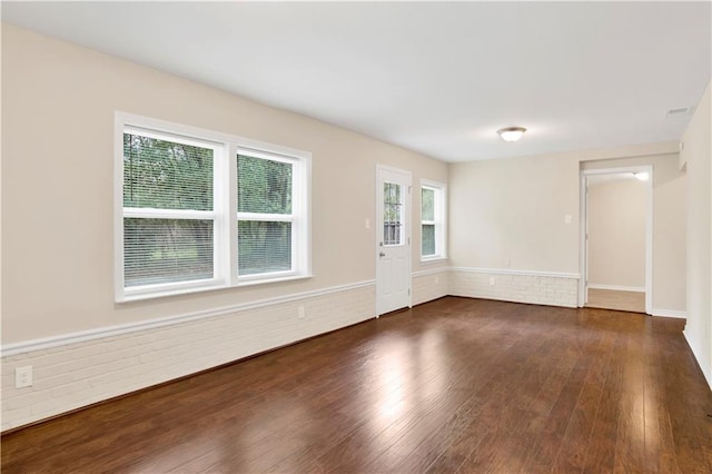 unfurnished room featuring brick wall and dark wood finished floors