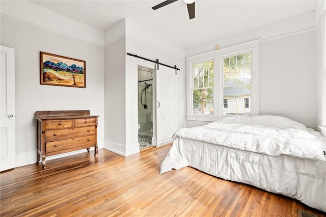 bedroom with ceiling fan, a barn door, connected bathroom, and hardwood / wood-style floors