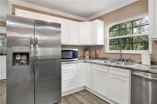 kitchen with appliances with stainless steel finishes, sink, white cabinets, ornamental molding, and light stone counters