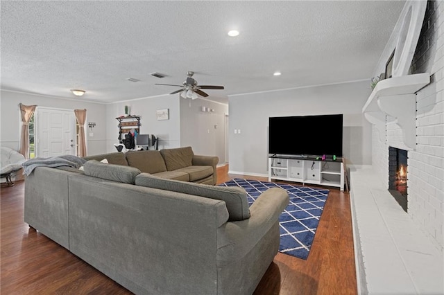 living room with ceiling fan, dark hardwood / wood-style flooring, a textured ceiling, and a brick fireplace