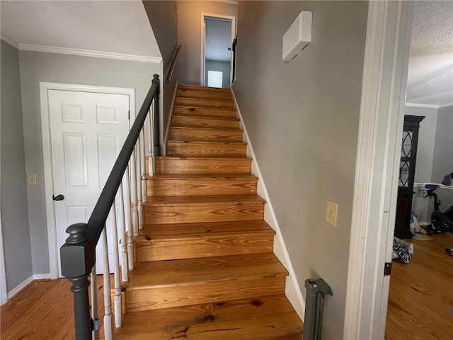 staircase with crown molding, wood finished floors, baseboards, and a textured ceiling