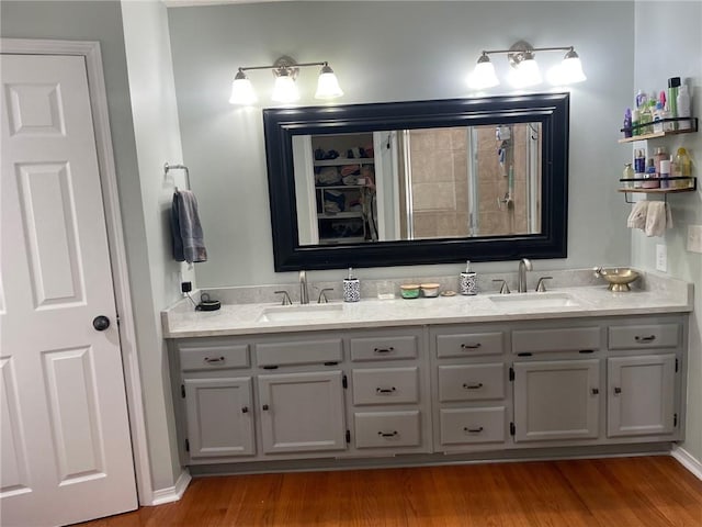 full bathroom with double vanity, a tile shower, wood finished floors, and a sink