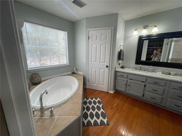 full bath featuring visible vents, a textured ceiling, wood finished floors, and a garden tub