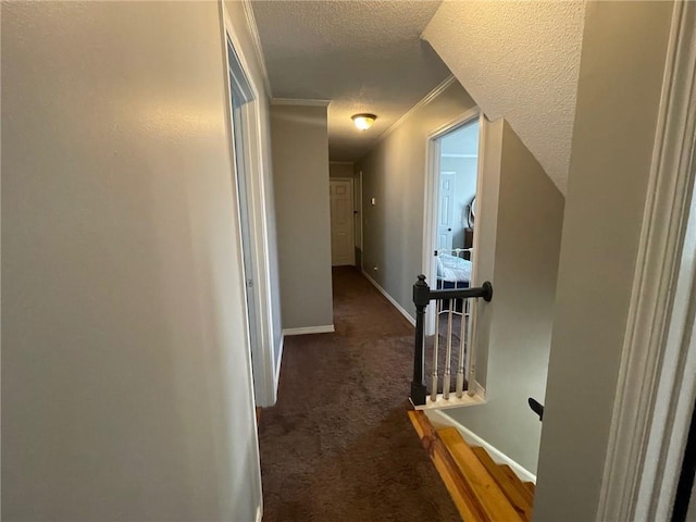 hall featuring baseboards, a textured ceiling, carpet, and ornamental molding