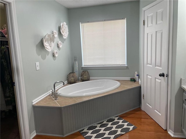 full bath featuring a bath, a healthy amount of sunlight, a spacious closet, and wood finished floors