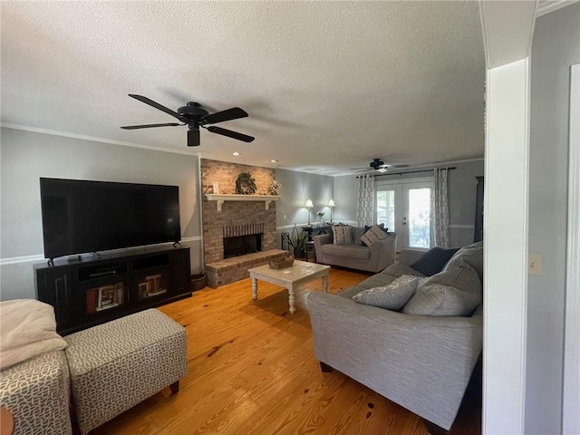 living area featuring a brick fireplace, a ceiling fan, light wood-style floors, and a textured ceiling