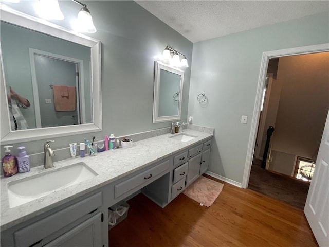 bathroom with a sink, a textured ceiling, wood finished floors, and double vanity