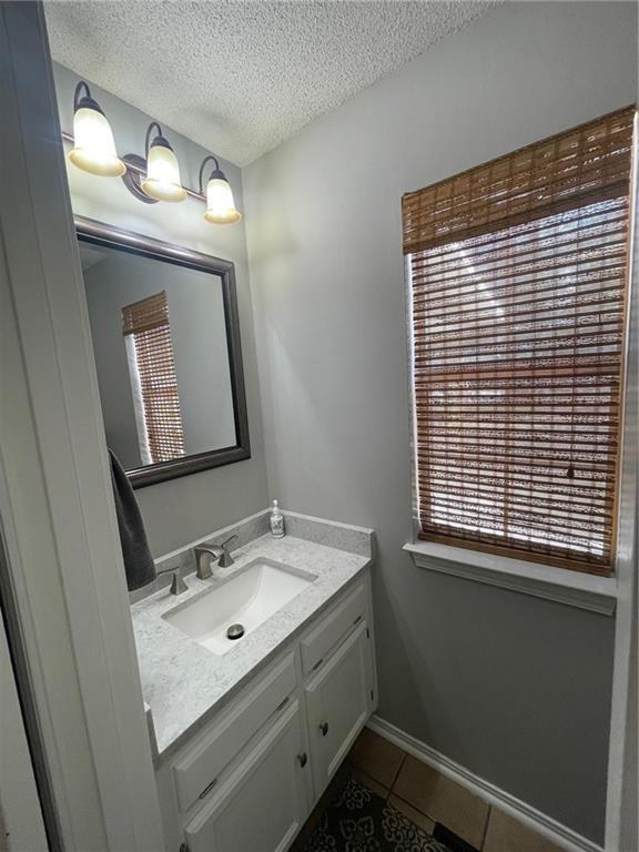 bathroom with vanity, tile patterned floors, baseboards, and a textured ceiling