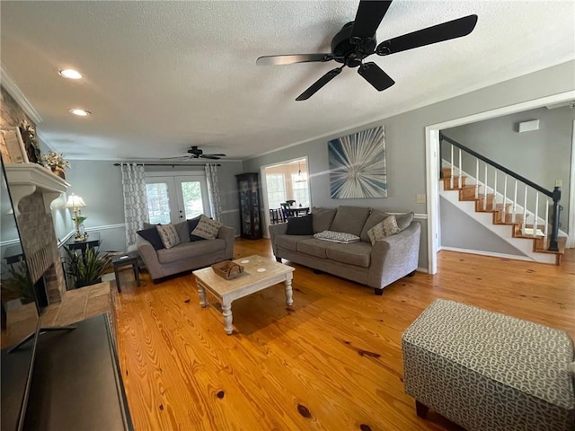 living area with stairway, wood finished floors, a fireplace with raised hearth, ceiling fan, and a textured ceiling