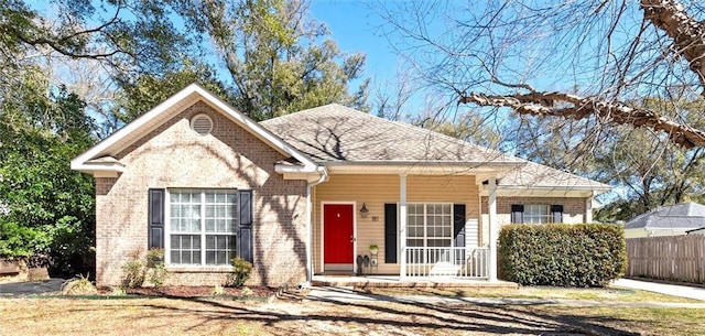 view of front of home featuring a shingled roof, covered porch, brick siding, and fence